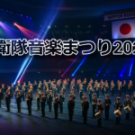日本武道館で行われる自衛隊音楽まつり2025の演奏シーン。青と赤のライトに照らされ、自衛隊音楽隊が整列して演奏している様子。